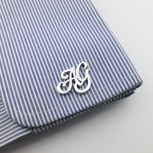 May include: Silver cufflinks with the letters "AG" in a stylized font.