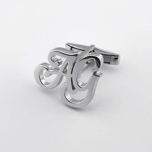 May include: Silver cufflinks with a stylized design of the letters "A" and "G" intertwined.