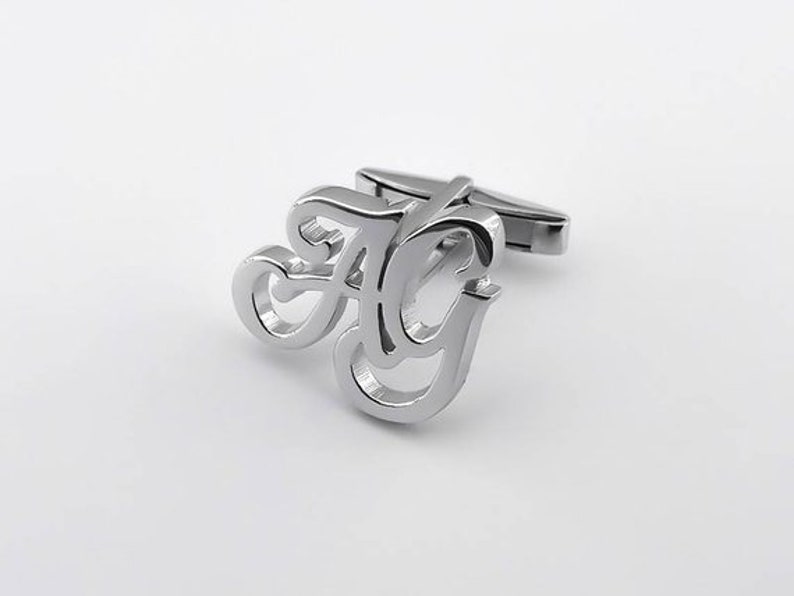 May include: Silver cufflinks with a stylized design of the letters "A" and "G" intertwined.