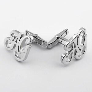 May include: Silver cufflinks with the letters "AG" in a cursive font.