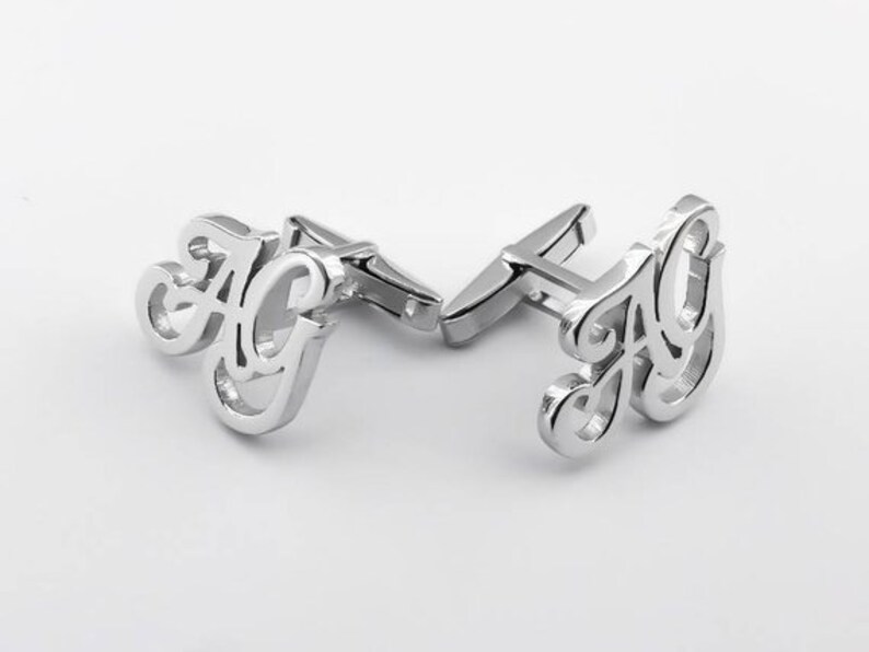 May include: Silver cufflinks with the letters "AG" in a cursive font.