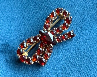 Broche em ouro amarelo maciço com lindo design de laço e pedras preciosas de granada.