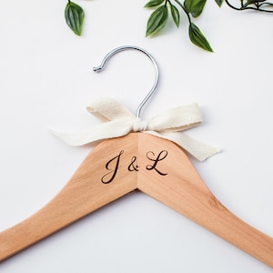 Peut inclure: Un cintre en bois avec un ruban blanc et les initiales "J & L" gravées sur le devant.