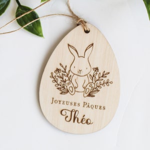 Peut inclure: Ornement de Pâques en bois en forme d'œuf avec un lapin et un motif floral. L'ornement est gravé avec le texte "Joyeuses Pâques Théo".