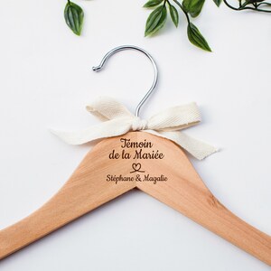 Peut inclure: Un cintre en bois avec un ruban blanc et le texte "Temoin de la Mariée" avec un symbole de cœur et "Stephane & Magalie" gravé dessus.