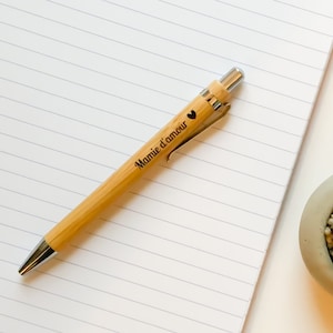 Peut inclure: Un stylo en bois avec un clip argenté et un cœur gravé sur le corps. Le stylo est gravé avec le texte "Mamie d'amour".