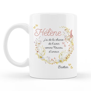 Peut inclure: Mug en céramique blanche avec un motif de couronne florale. Le mug présente le texte "Hélène j'ai de la chance de t'avoir comme Nounou d'amour Bastien" en lettres roses et jaunes.