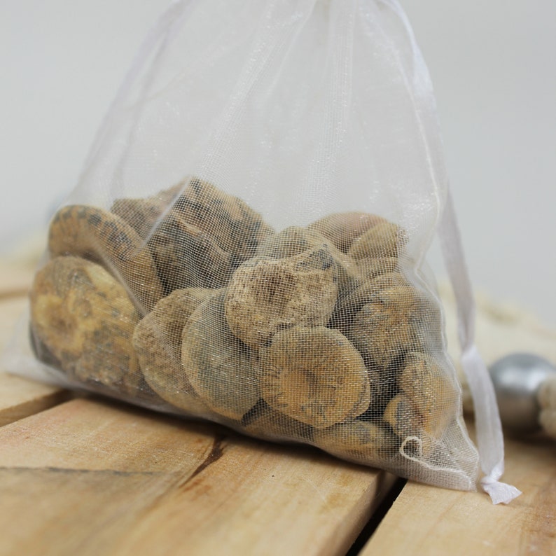 May include: A white mesh bag filled with a variety of small, brown, fossilised shells. The bag is sitting on a wooden surface.