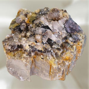 Puede incluir: Un espécimen mineral en bruto que presenta un grupo de cristales de cuarzo translúcidos y dentados en tonos claros, gris ahumado y ámbar. La base consiste en roca sólida y opaca de color tostado con manchas minerales de color naranja.