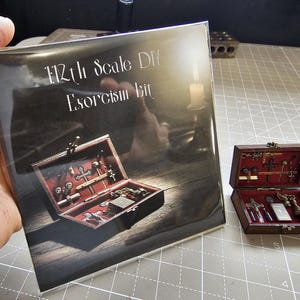 May include: A brochure and a miniature wooden box with a red interior, containing small religious items. The brochure reads "1/12th Scale DIY Exorcism Kit". The box is open, displaying crosses, keys, and other detailed miniature accessories.