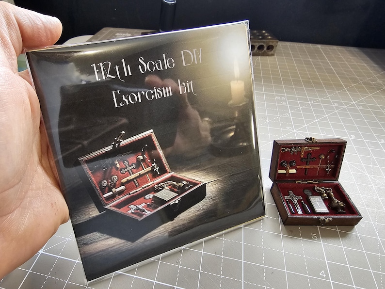 May include: A brochure and a miniature wooden box with a red interior, containing small religious items. The brochure reads "1/12th Scale DIY Exorcism Kit". The box is open, displaying crosses, keys, and other detailed miniature accessories.