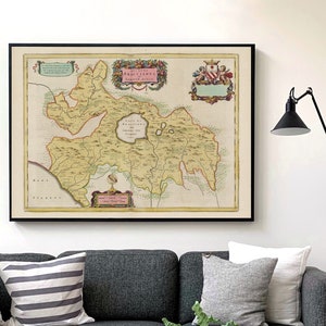 Può includere: Interno di un soggiorno con un divano grigio, cuscini e un tavolino in legno. Una mappa antica incorniciata è appesa al muro. Sono visibili anche una lampada nera e un tavolino con un vaso bianco. Il tappeto ha un motivo geometrico.