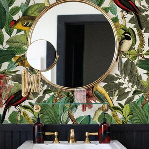 May include: A white porcelain bathroom sink with gold faucets and a black and white tiled wall behind it. The wall is decorated with a wallpaper featuring a floral pattern with birds and leaves. The wallpaper is cream colored with green leaves, red flowers, and yellow birds. The text "THE GOODIES." is visible in the bottom right corner of the image.