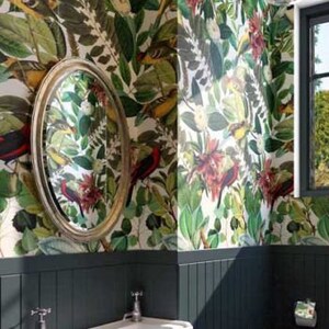 May include: A small bathroom with dark green walls and a white porcelain sink and toilet. The walls are covered in a wallpaper with a tropical print featuring birds and flowers. A glass globe light fixture hangs from the ceiling.