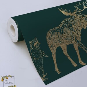 May include: A roll of dark green wallpaper with a gold foil pattern of a moose, raccoon, and other forest animals. The wallpaper is printed with a textured, hand-drawn style.