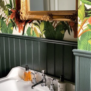 May include: A white porcelain bathroom sink with a chrome faucet and two soap dispensers. The sink is set against a dark green wood panel wall with a floral wallpaper border.