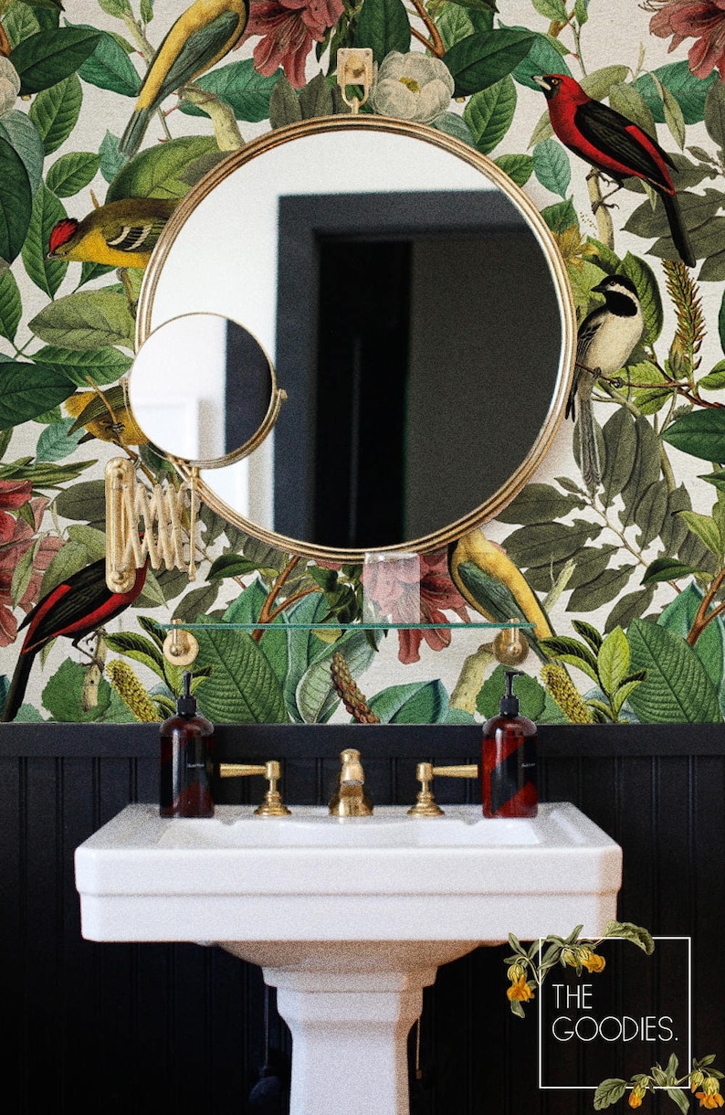 May include: A white porcelain bathroom sink with gold faucets and a black and white tiled wall behind it. The wall is decorated with a wallpaper featuring a floral pattern with birds and leaves. The wallpaper is cream colored with green leaves, red flowers, and yellow birds. The text "THE GOODIES." is visible in the bottom right corner of the image.