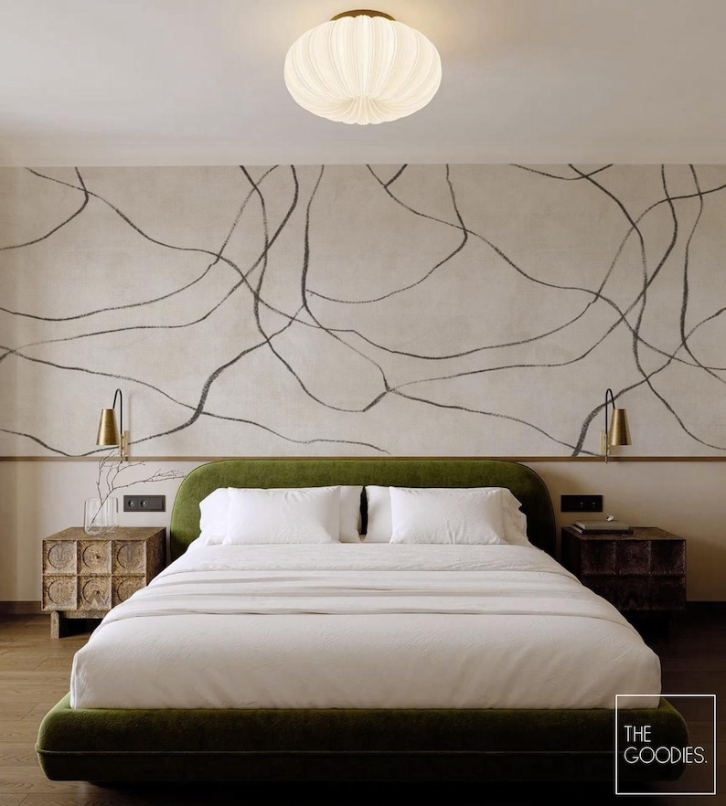 Op de afbeelding: Slaapkamer met een groen gestoffeerd bed en wit beddengoed, geflankeerd door houten nachtkastjes. De muur achter het bed is neutraal met zwarte abstracte lijnen. Een witte, geribbelde plafondlamp en messing wandkandelaars maken het decor compleet.