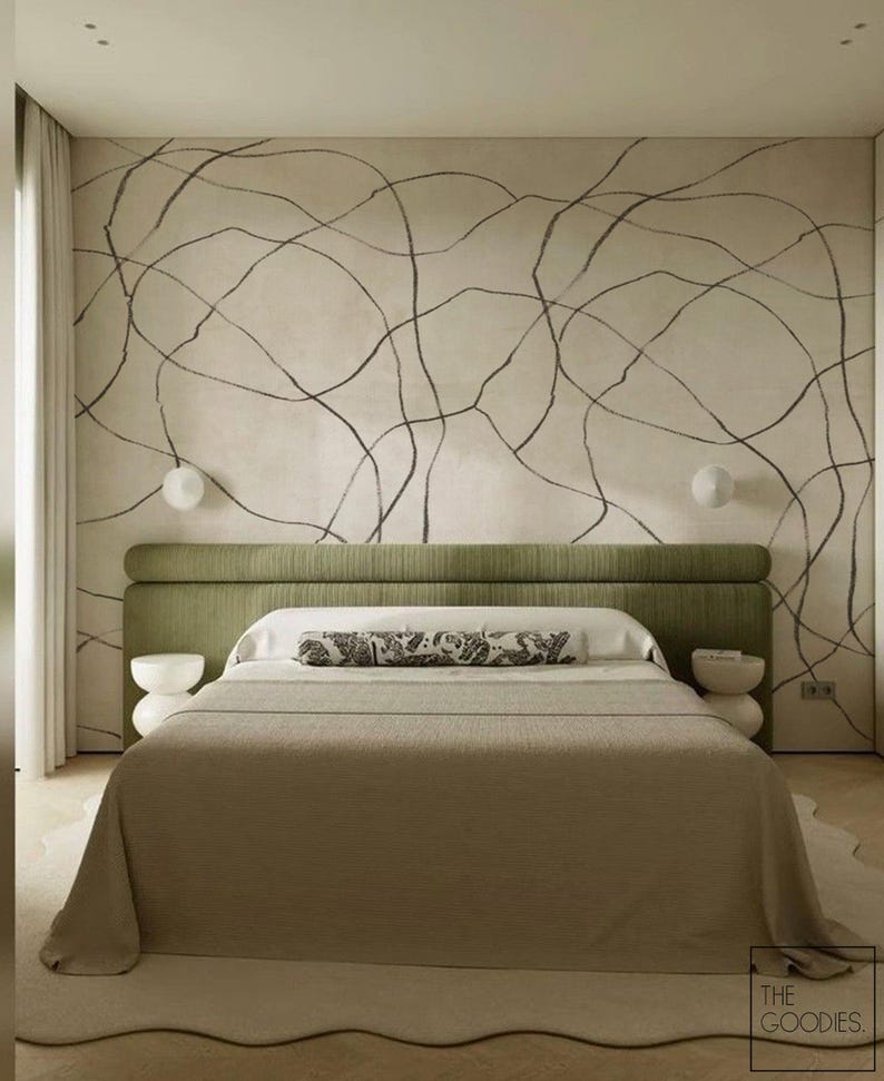 Op de afbeelding: Een moderne slaapkamer met een bed met een groen hoofdbord en een deken in neutrale tinten. De muur achter het bed is cr&egrave;mekleurig met zwarte abstracte lijnen. Twee witte nachtkastjes en een decoratief kussen maken de sc&egrave;ne compleet.