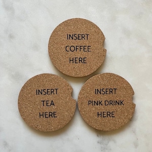 May include: Three round cork coasters with a cutout for a beverage. The coasters have the text "Insert Coffee Here", "Insert Tea Here", and "Insert Pink Drink Here" printed on them.