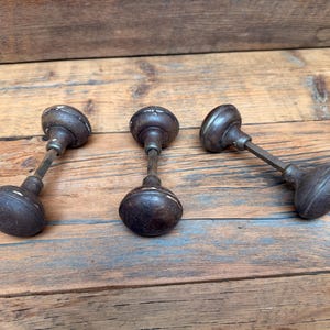May include: Three dark brown, round door knobs with visible wear and chipped paint. Each knob is attached to a central metal spindle, featuring a classic spherical shape and a weathered, textured surface that shows signs of age and use.