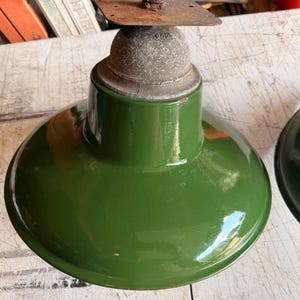 May include: A glossy forest green enamel pendant light shade with a wide, flared rim. The top features a weathered, textured gray metal socket housing with a flat, rusted mounting plate attached to the top, showing signs of age and wear.