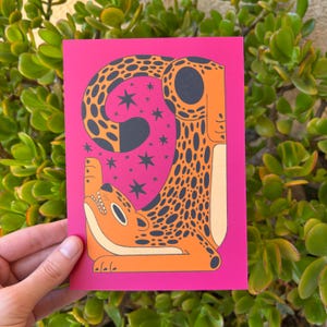 Pu&ograve; includere: Uno sfondo rosa con un'illustrazione stilizzata di un leopardo con macchie arancioni e nere. Il leopardo &egrave; rannicchiato con la coda in bocca. Lo sfondo &egrave; pieno di stelle bianche.
