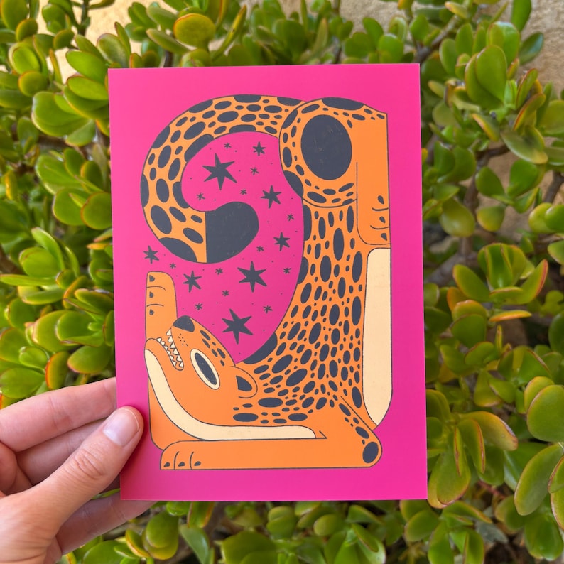 Pu&ograve; includere: Uno sfondo rosa con un'illustrazione stilizzata di un leopardo con macchie arancioni e nere. Il leopardo &egrave; rannicchiato con la coda in bocca. Lo sfondo &egrave; pieno di stelle bianche.