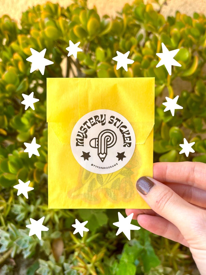 K&ouml;nnte beinhalten: Ein gelber Papierumschlag mit einem runden Aufkleber mit der Aufschrift "MYSTERY STICKER". Der Aufkleber zeigt einen Bleistift und Sterne. Wei&szlig;e Sterne umgeben den Umschlag, vor einem Hintergrund aus gr&uuml;nen Bl&auml;ttern.