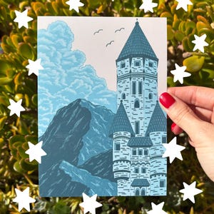 May include: A blue and white print of a castle with a mountain range and clouds in the background. The castle has multiple turrets and a tall central tower. Three birds fly above the castle. The print is surrounded by white star cutouts.