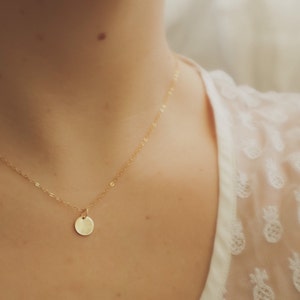 May include: A delicate gold chain necklace with a small, round pendant. The pendant is smooth and has a subtle shine.