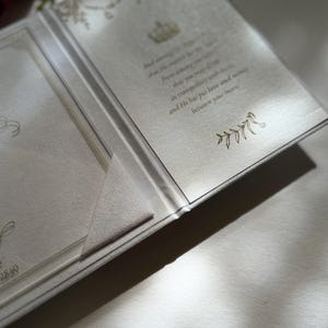 May include: A white invitation card with a gold design and text that reads "And he shall send his angel before you to guard you on your way and to bring you to the place that I have prepared for you. In tranquility you will enter and he has put love and mercy between you and your heart."