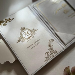 May include: A white wedding invitation with gold foil detailing. The invitation features a monogram with the initials "M & S" and the text "Mohammad and Salam, August 18, 2024".