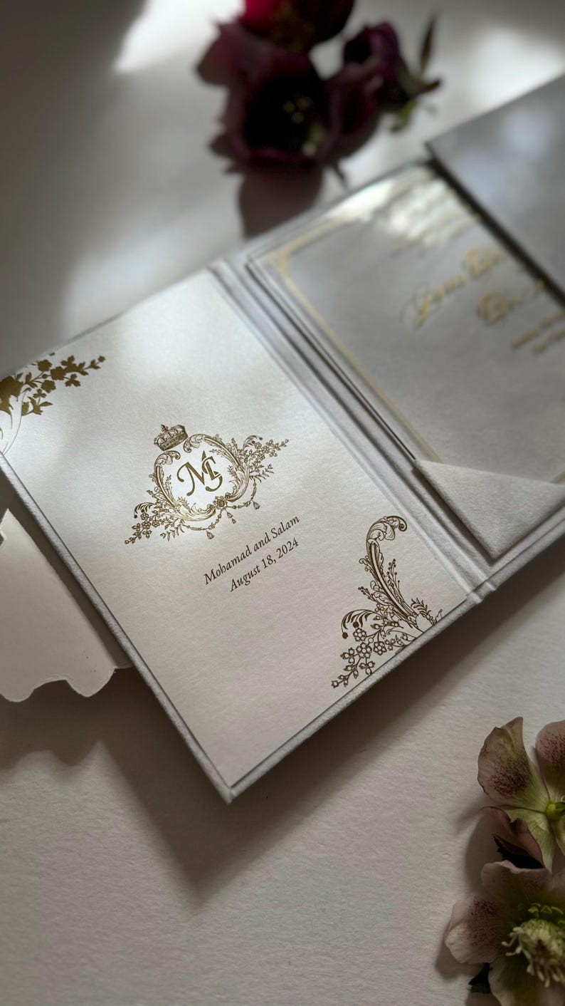 May include: A white wedding invitation with gold foil detailing. The invitation features a monogram with the initials "M & S" and the text "Mohammad and Salam, August 18, 2024".