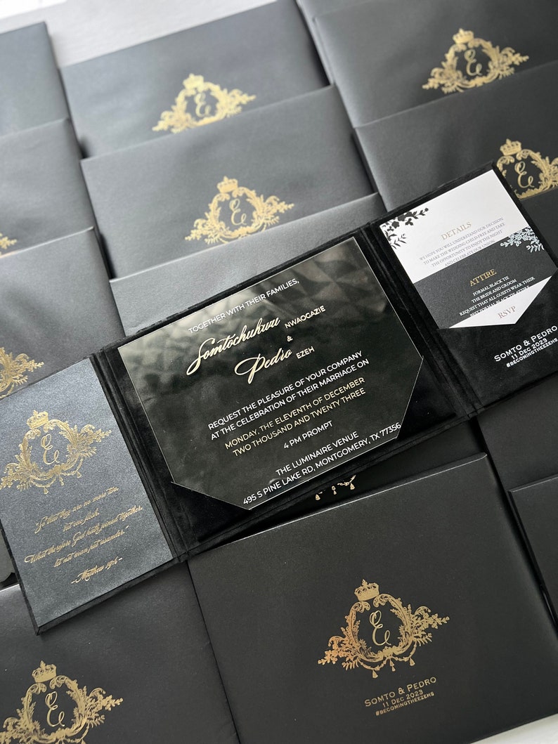 May include: Black and gold wedding invitation with a clear acrylic cover. The invitation features a gold crest with the letter "E" and the text "Somtechukuru & Pedio" and the date "11 Dec 2023". The invitation also includes the text "Together with their families, Somtechukuru Nwaogazie & Pedio Ezeh" and the details of the wedding ceremony.
