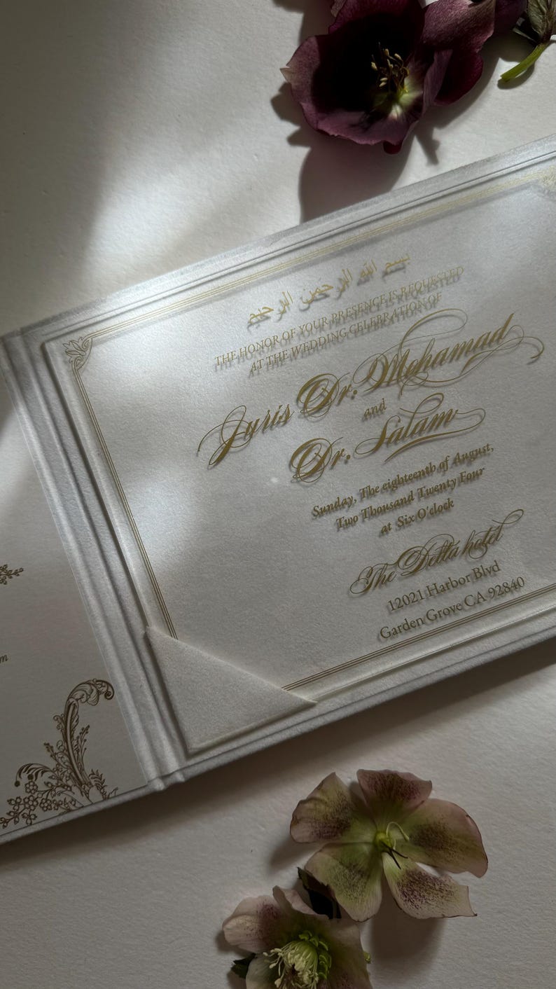 May include: A white wedding invitation with gold lettering. The invitation announces the wedding of Juris Dr. Mhamad and Dr. Salam. The wedding will take place on Sunday, the eighteenth of August, Two Thousand Twenty Four at Six O'clock at The Bella Hotel, 12021 Harbor Blvd, Garden Grove CA 92840.