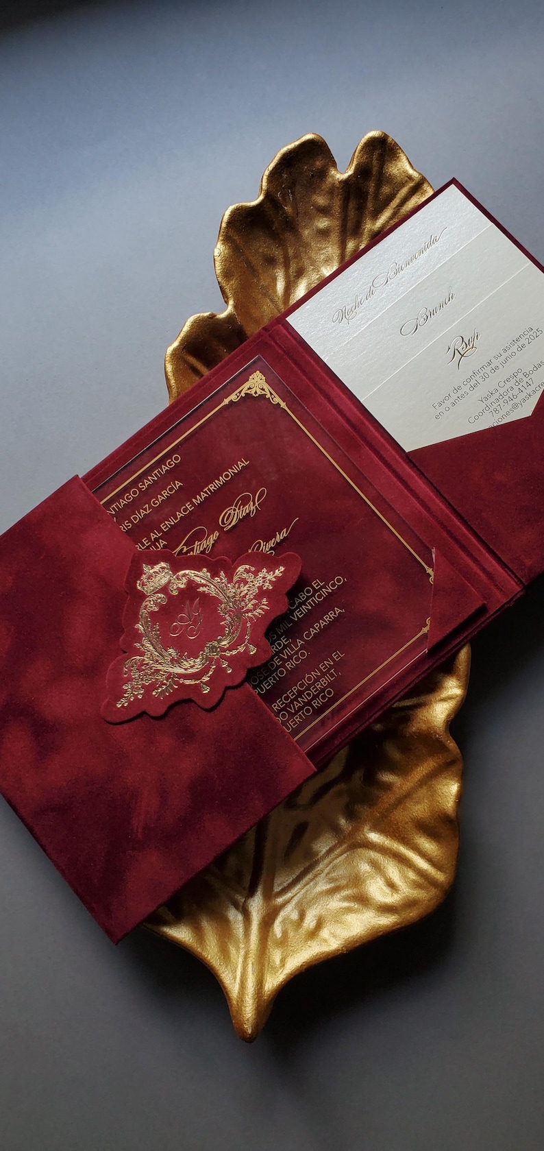 May include: Burgundy wedding invitation with gold accents, featuring a gold embossed emblem and elegant script. The invitation is presented on a gold leaf-shaped tray, creating a luxurious aesthetic.