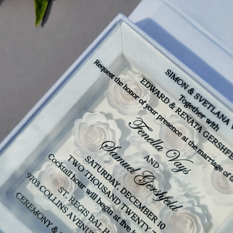Puede incluir: Una tarjeta de invitaci&oacute;n blanca con una cubierta de pl&aacute;stico transparente. La tarjeta presenta un dise&ntilde;o de flores de papel blanco y el texto "Request the honor of your presence at the marriage of Simon & Svetlana Together with Edward & Renata Gershfeld Fenella Vays and Samuel Gershfeld Saturday, December 10 Two Thousand Twenty Cocktail hour will begin at five St. Regis Bal 9703 Collins Avenue Ceremony &"