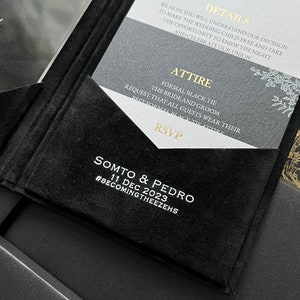 May include: A black and white wedding invitation with gold accents. The invitation features the text "Details", "Attire", "RSVP", "Somto & Pedro", "11 Dec 2023", and "#BecomingTheezehs".