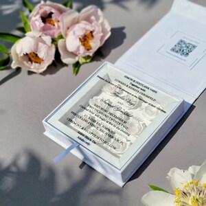 Puede incluir: Una invitaci&oacute;n de boda blanca con una cubierta de acr&iacute;lico transparente con un dise&ntilde;o floral. El texto de la invitaci&oacute;n dice: "Request the honor of your presence at the marriage of their children Simon & Svetlana Vays Together with Edward & Renata Gershfeld Fenella Vays and Samud Gerhfeld Saturday, December 10 Two Thousand Twenty Two Cocktail hour will begin at five in the evening St. Regis Bal Harbour 9703 Collins Avenue, Bal Harbour, FL Ceremony & Reception to Follow Attire: Black Tie Adults only"