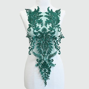 May include: Teal green floral lace applique with sequins. The applique features a delicate floral design with intricate details. It is perfect for adding a touch of elegance to any garment or project.