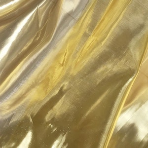 May include: A close-up of a gold sheer fabric with a subtle shimmer. The fabric is wrinkled and has a soft, flowing texture.