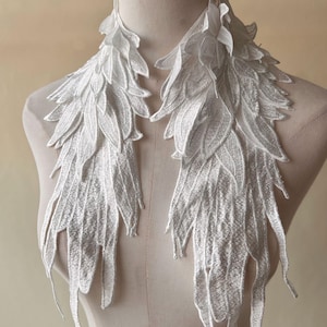 May include: White lace trim with a feather design. The trim is made of delicate, white lace and features a layered feather pattern. It is perfect for adding a touch of elegance to any project.