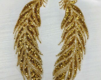 May include: Two gold sequined feather appliques. The feathers are detailed with a delicate, intricate design and are perfect for adding a touch of sparkle to any project.