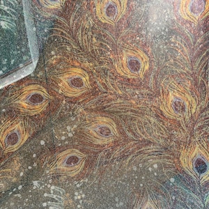 May include: A close-up of a fabric with a peacock feather pattern. The feathers are a mix of brown, gold, and yellow with a hint of blue. The fabric has a textured, almost iridescent look.
