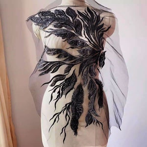 May include: Black lace applique with a floral design featuring intricate details and beading. The applique is on a sheer mesh background.