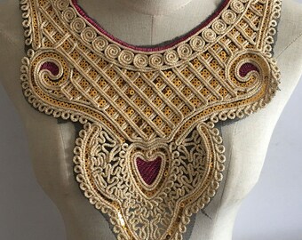 May include: Gold and burgundy sequined lace trim with a scalloped edge. The trim is designed to be used as a neckline embellishment for clothing.