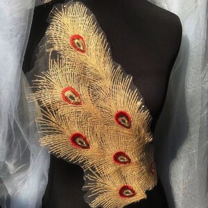May include: Gold and red peacock feather embroidery applique. The applique features a design of several peacock feathers with red eyes and gold glitter.
