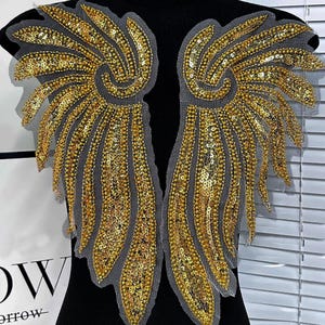 Op de afbeelding: Een paar gouden paillettenvleugels met een mesh-rug. De vleugels zijn ontworpen om op kleding te worden genaaid.