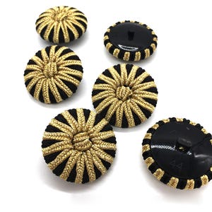 May include: Six black and gold striped fabric buttons. The buttons have a raised center and a flat back. The buttons are approximately 1 inch in diameter.